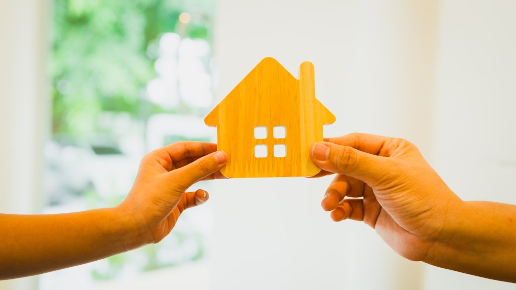 Zwei Hände halten gemeinsam ein Modell eines Holzhauses