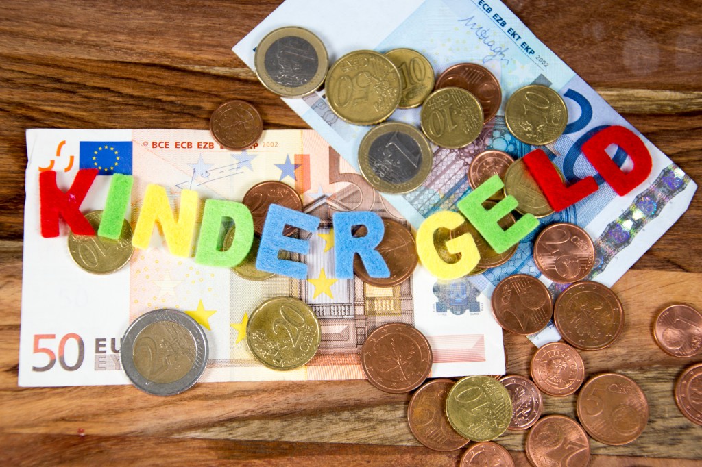 Geldscheine und Münzen. Bunte Buchstaben mit dem Text "Kindergeld"